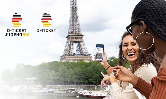 Zwei junge Frauen in Paris halten ihr Handy mit D-Ticket in die Kamera. Im Hintergrund sieht man den Eiffelturm