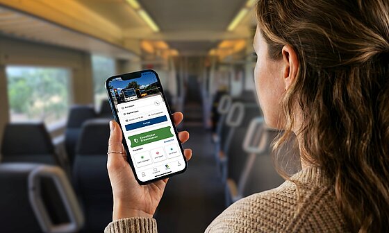Junge Frau sitzt in Regionalbahn und schaut auf Ihr Handy mit geöffneter naldo-App