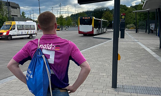 Junger Mann mit naldo-WM-Shirt und naldo-Rucksack steht am Tübinger Busbahnhof